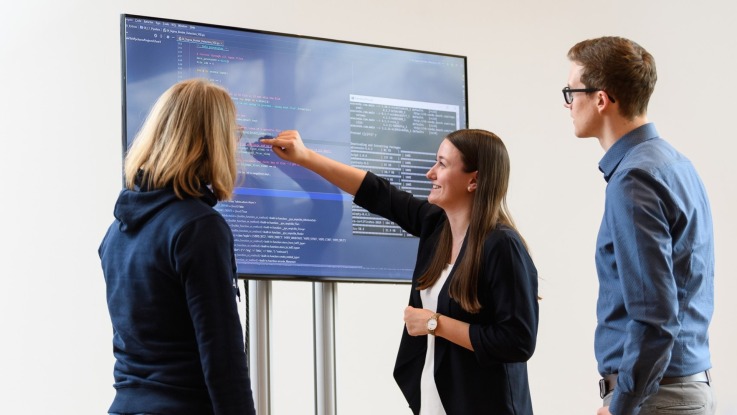 Mehrere Mitarbeiter diskutieren vor einem Bildschirm über die darauf gezeigten Programmierungen
