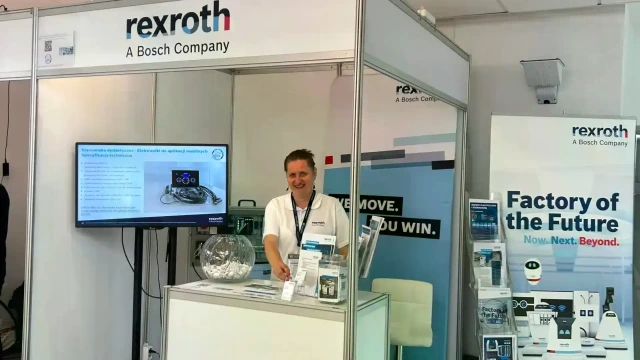 A woman at the Bosch Rexroth booth with a multimedia presentation, roll-ups, and brochures.