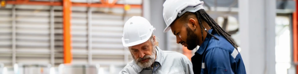 Generationsmöte i verkstaden där en äldre kollega delar kunskap med en yngre medarbetare.