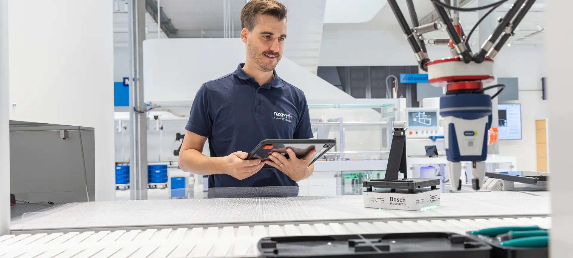Bosch Rexroth çalışanı, dijital fabrika ortamında robotik kol ile üretim sürecini tablet üzerinden kontrol ediyor.