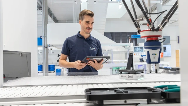 Bosch Rexroth çalışanı, dijital fabrika ortamında robotik kol ile üretim sürecini tablet üzerinden kontrol ediyor.