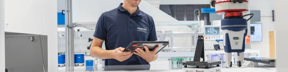 Bosch Rexroth çalışanı, dijital fabrika ortamında robotik kol ile üretim sürecini tablet üzerinden kontrol ediyor.
