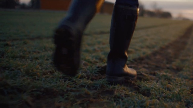 Person in boots walking on a green field.