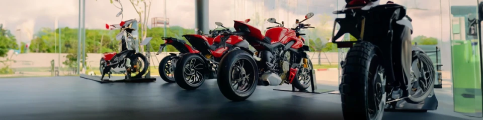 Motos Ducati em fila em uma concessionária com árvores ao fundo.