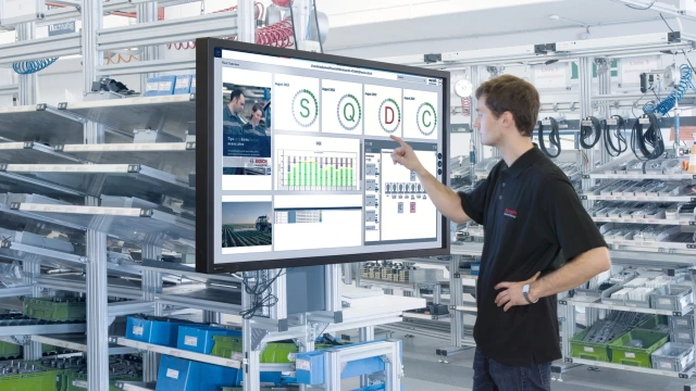 A man in a factory checking processes on a large screen.