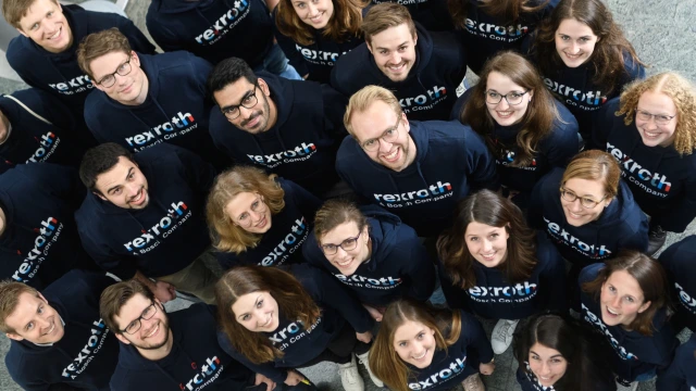 A diverse group of people all with Rexroth sweaters on are staring up into the camera and smiling.