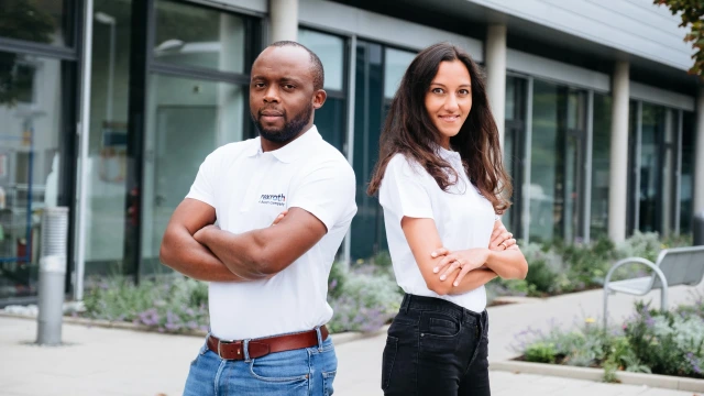 Two diverse people, one man and one woman have their arms crossed, leaning against each other back to back and smiling.