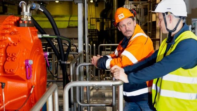 Two men in safety helmets standing infront of a red Hägglunds motor.