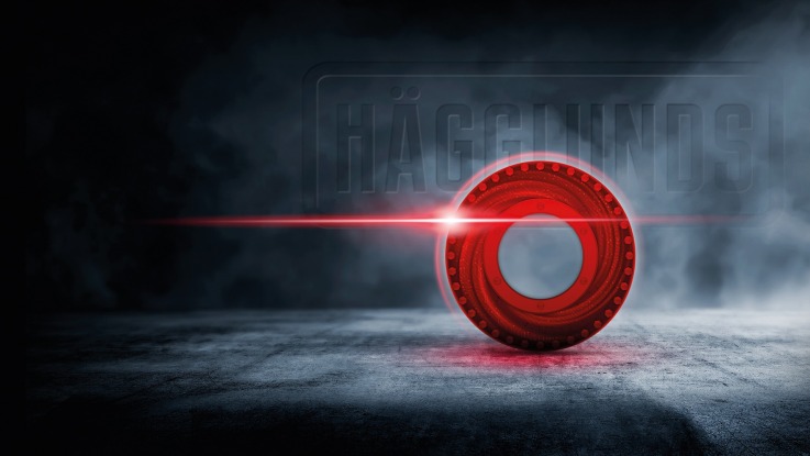 Red Hägglunds core symbol on concrete floor with the Hägglunds logo in a smokey background.