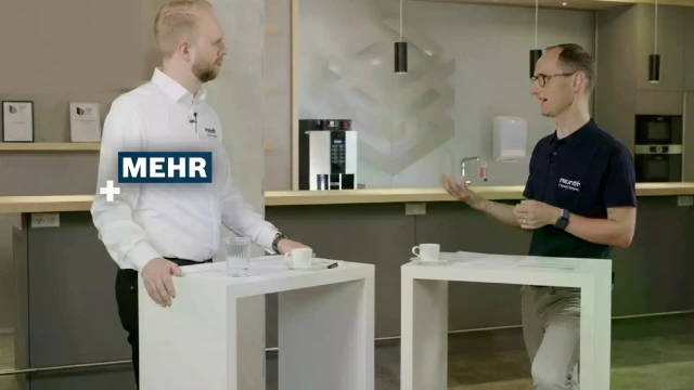 Two people talking with the ‘+MEHR’ logo