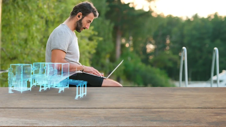 Man working on laptop with a holographic CAD design.