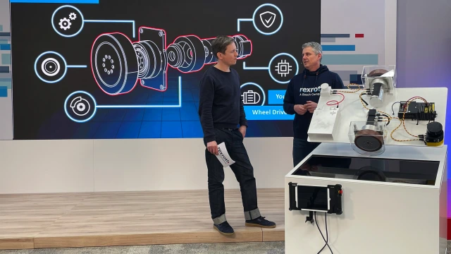 Joerg Heckel (Director de Nuevos Negocios de Bosch Rexroth) y un moderador se encuentran delante del expositor de ROKIT-ctrlX AUTOMATION mientras muestran en detalle el ROKIT Motor.