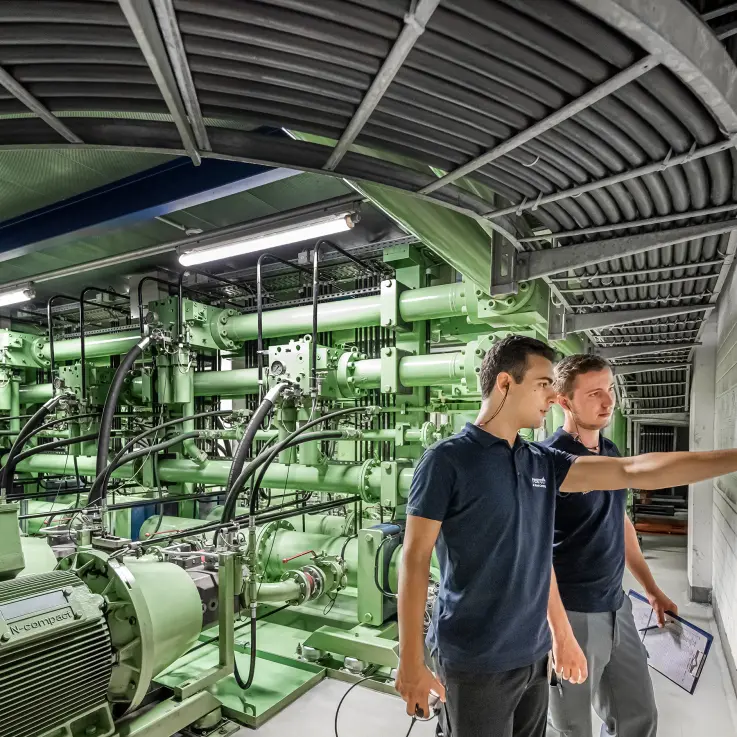 Two men standing in a factory with green machines in the Background