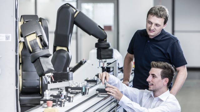 Dva muži před výrobní linkou konfigurují robota APAS 