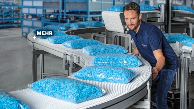 Associate at VarioFlow belt, which transports numerous bags. The motto "MORE+" can also be read.