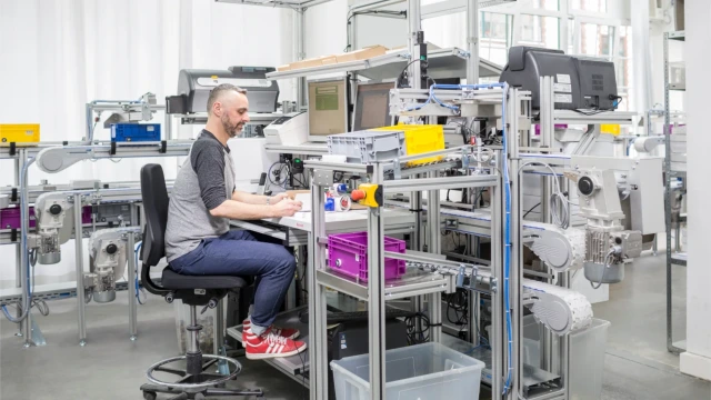 Mann arbeitet an einer Werkbank, ein Fördersystem liefert Materialien.