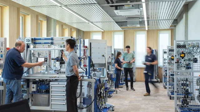 Training situation with trainer and participants during a practical exercise in front of the Hydraulix 300 training system at the Bosch Rexroth Academy's Ulm training center.