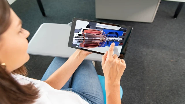 A Bosch Rexroth Academy participant holds a tablet during a theory training session. The tablet displays a hydraulic animation of a directional control valve.